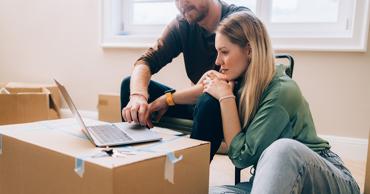 A couple reviews information on their laptop computer, which is placed on top of a sealed moving box.