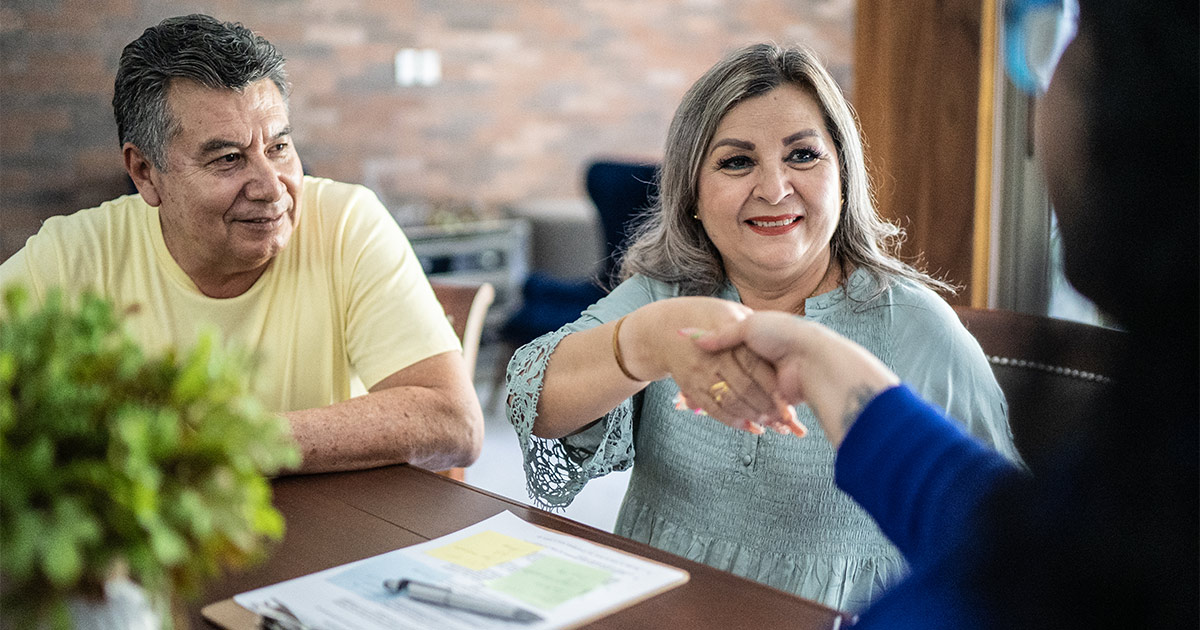 A mortgage banker shakes hands with two happy clients after they sign a document. They have just enjoyed a robust set of experienced closing services.