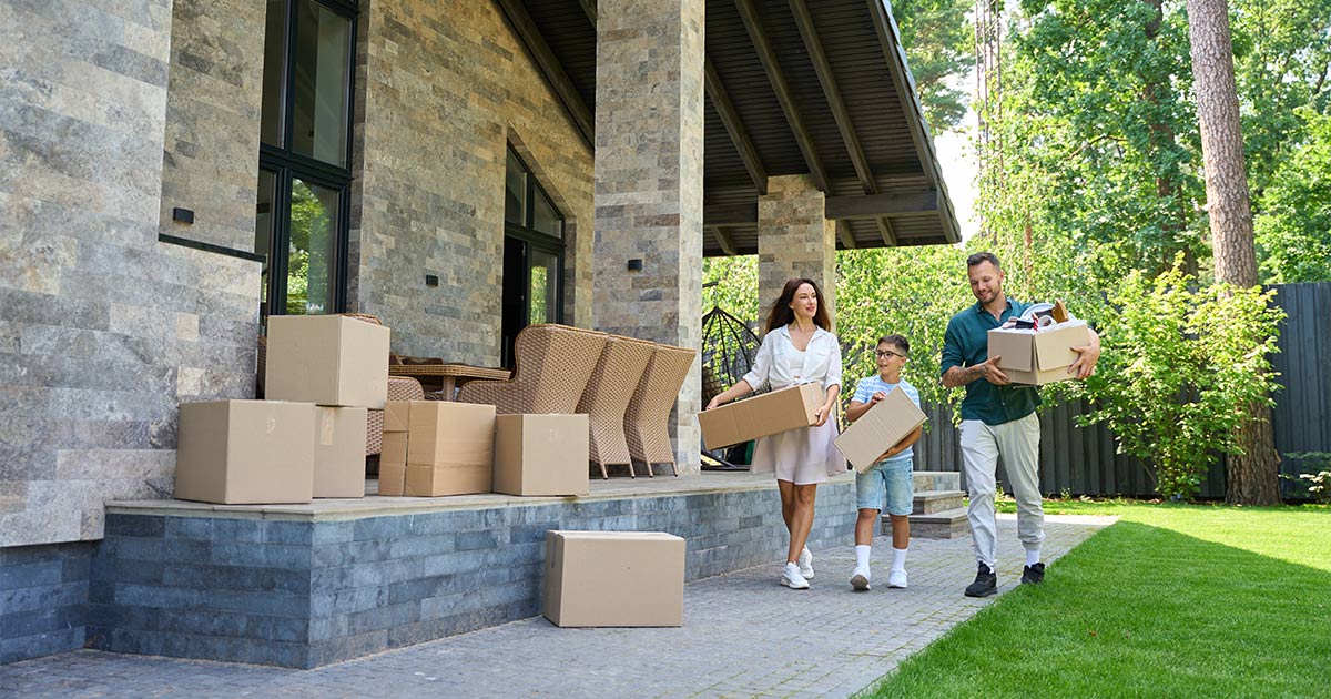 A family of three carries boxes as they move out of their home during peak moving season.